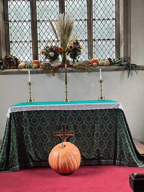 A church old tile decorated for harvest festival, with a large pumpkin and cross in front.