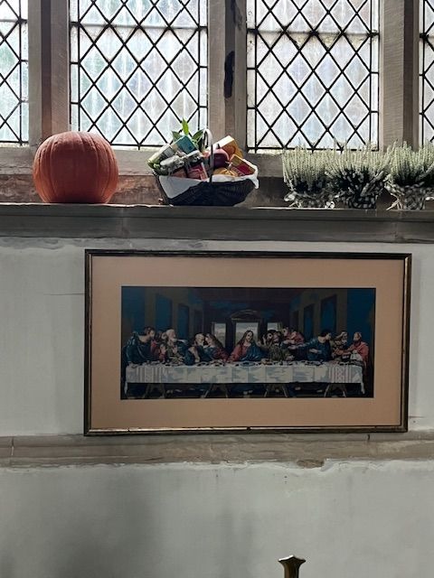 A framed print of "The Last Supper", displayed on a ledge below a windowsill decorated with harvest items.