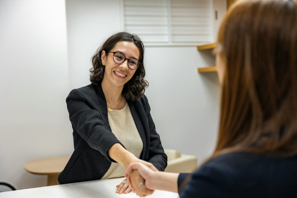 A professional woman shaking hands with across a table with another woman
